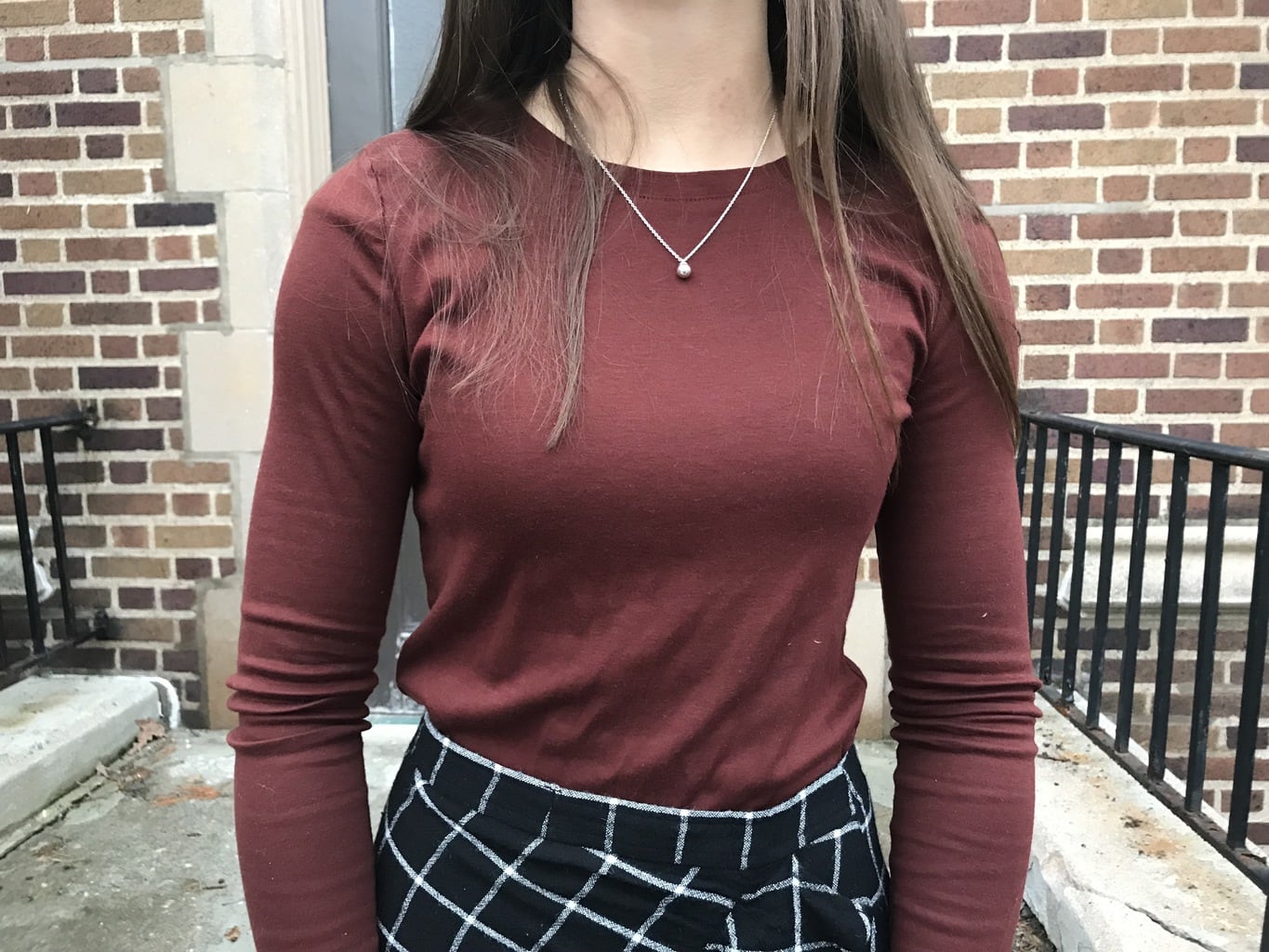 Jillian wears a soft, long sleeve, maroon crew neck shirt tucked into her black skirt.