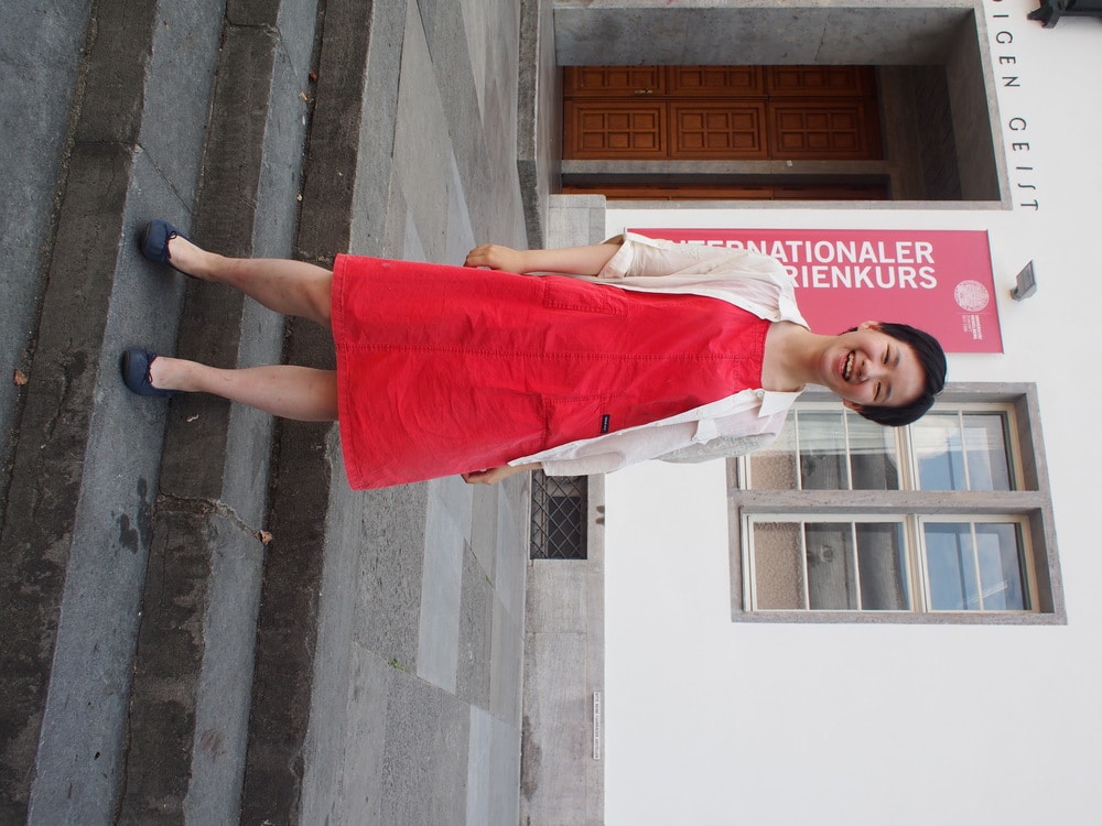 Victoria, a student at Science Po, wears a red utilitarian dress with navy ballet flats and a tan button-up on top.