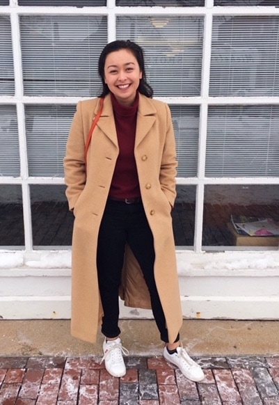 Suffolk University student Shannon looks stylish in the cold. She wears an ankle-length tan peacoat over a maroon turtleneck with belted black jeans and white sneakers.