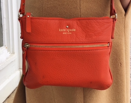 This bright orange Kate Spade crossbody mini purse jhas gold accents and zippers.