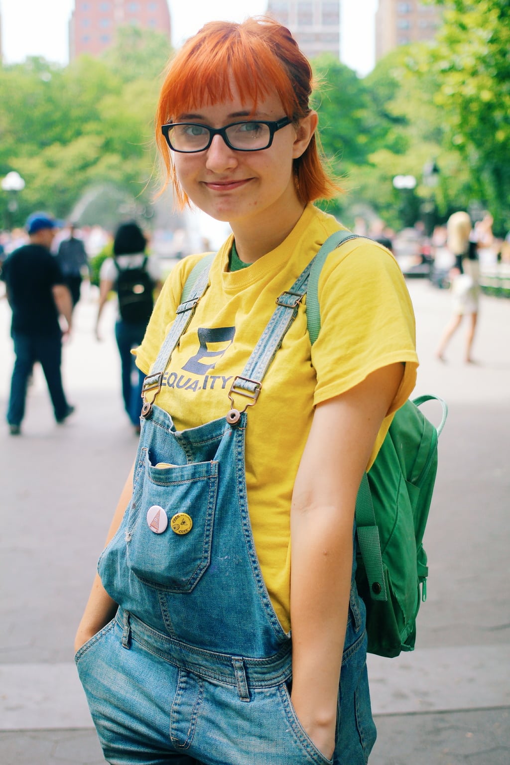 Fashion at School of Visual Arts, NYC - student Kaylee rocks bright red hair, a yellow Equality tee shirt, a green backpack, and overall shorts