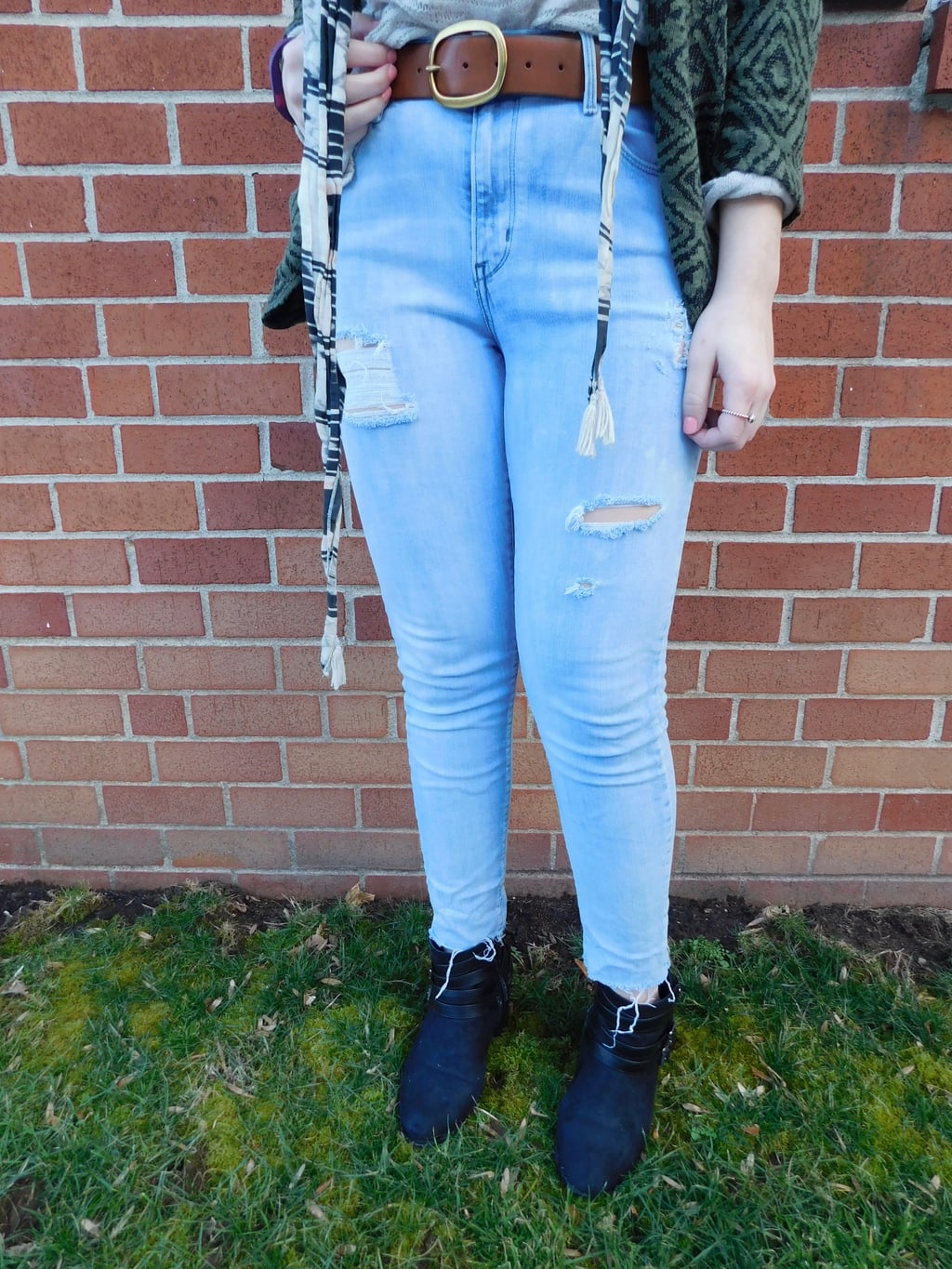 Lauren's light-wash, high waisted distressed denim jeans are held up by a thick brown belt with a gold buckle.