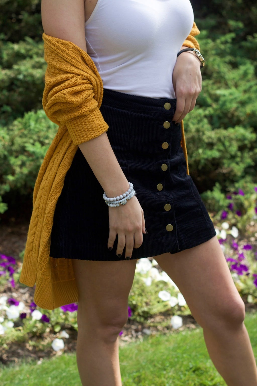 University of Bridgeport student wearing a chunky, slouchy mustard knit cardigan with a navy button-front high-waisted miniskirt and a white camisole tucked in.