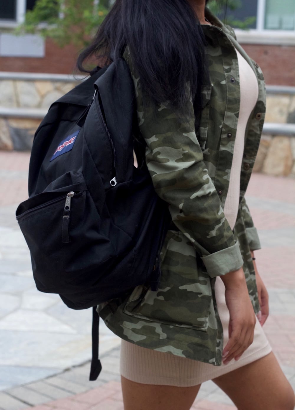 Mix and match: student totes around a black carryall Jansport backpack with her camouflage rain jacket and beige mini dress.