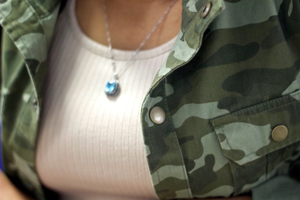 Detail of camouflage jacket over a nude dress with a simple aqua necklace on a silver chain.