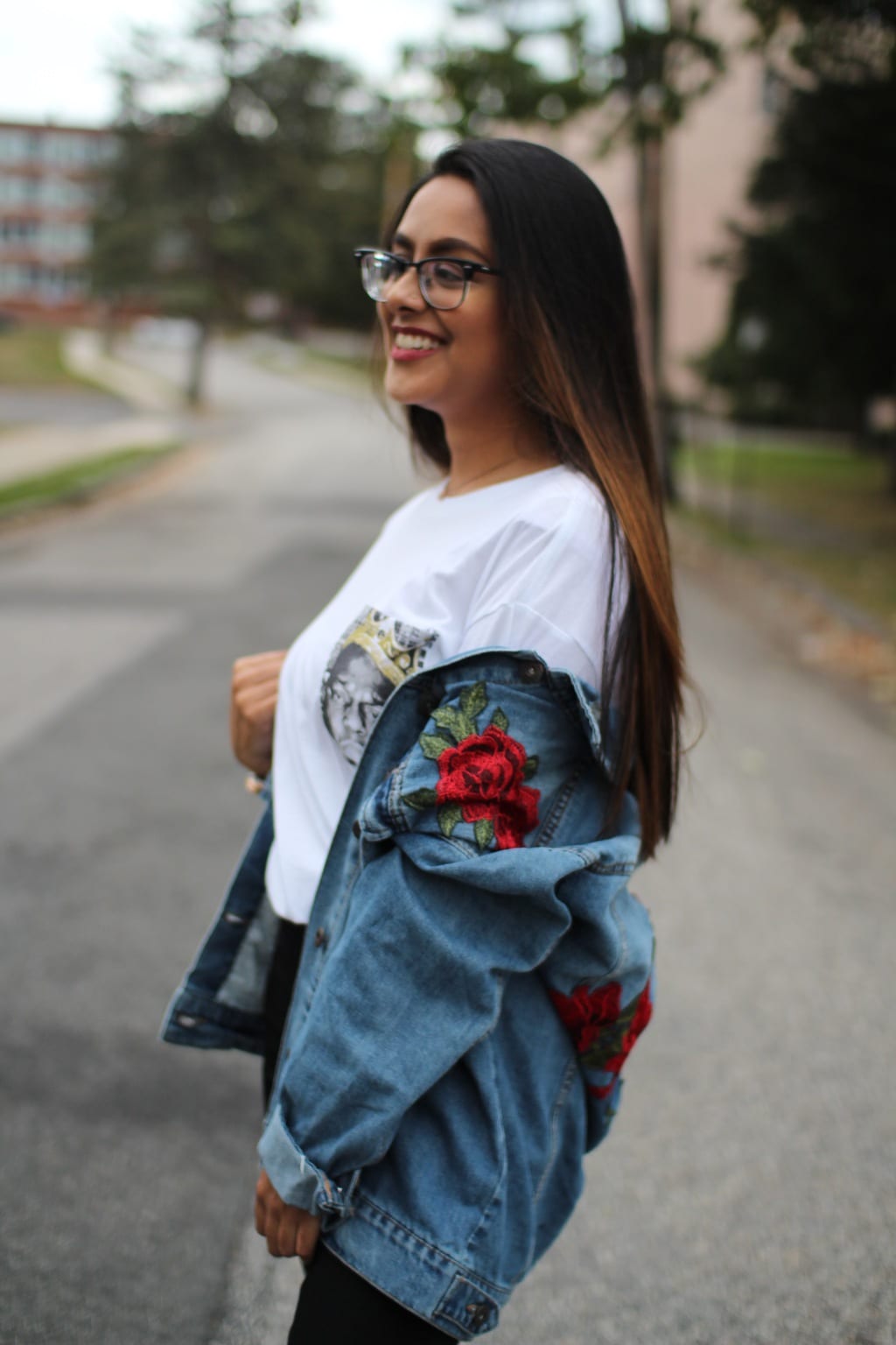 This oversized, distressed denim jacket is embroidered with red roses with green leaves. She wears it with a simple white tee.