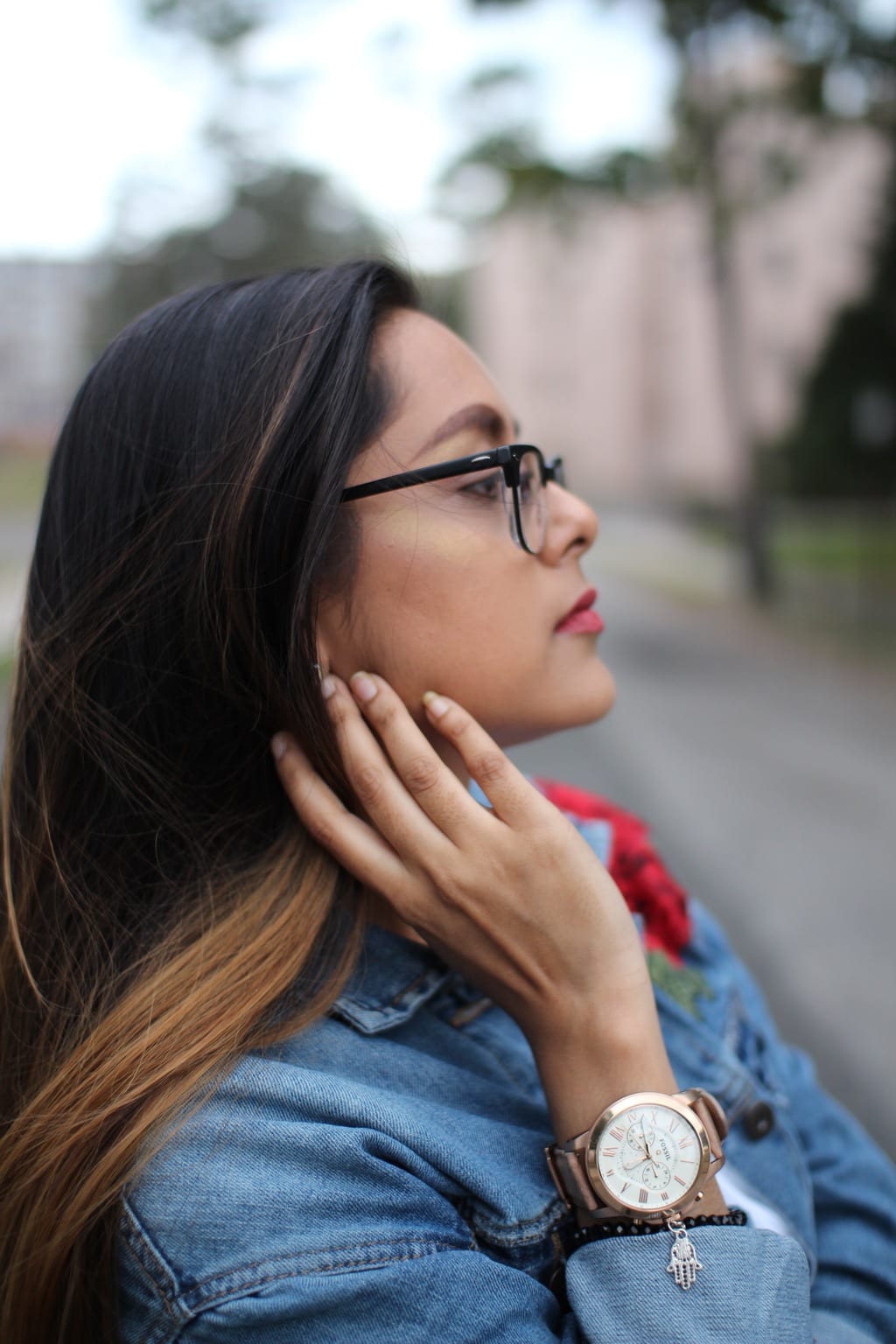 A University of Bridgeport student wears a large whitefaced, rosegold watch with a black beaded bracelet and an oversized denim embroidered jacket.