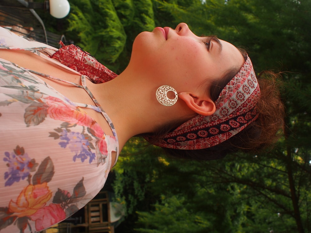 Amy sports a light blue, pink, and black paisley print bandana tied around her head and silver hoop earrings with cutout details.