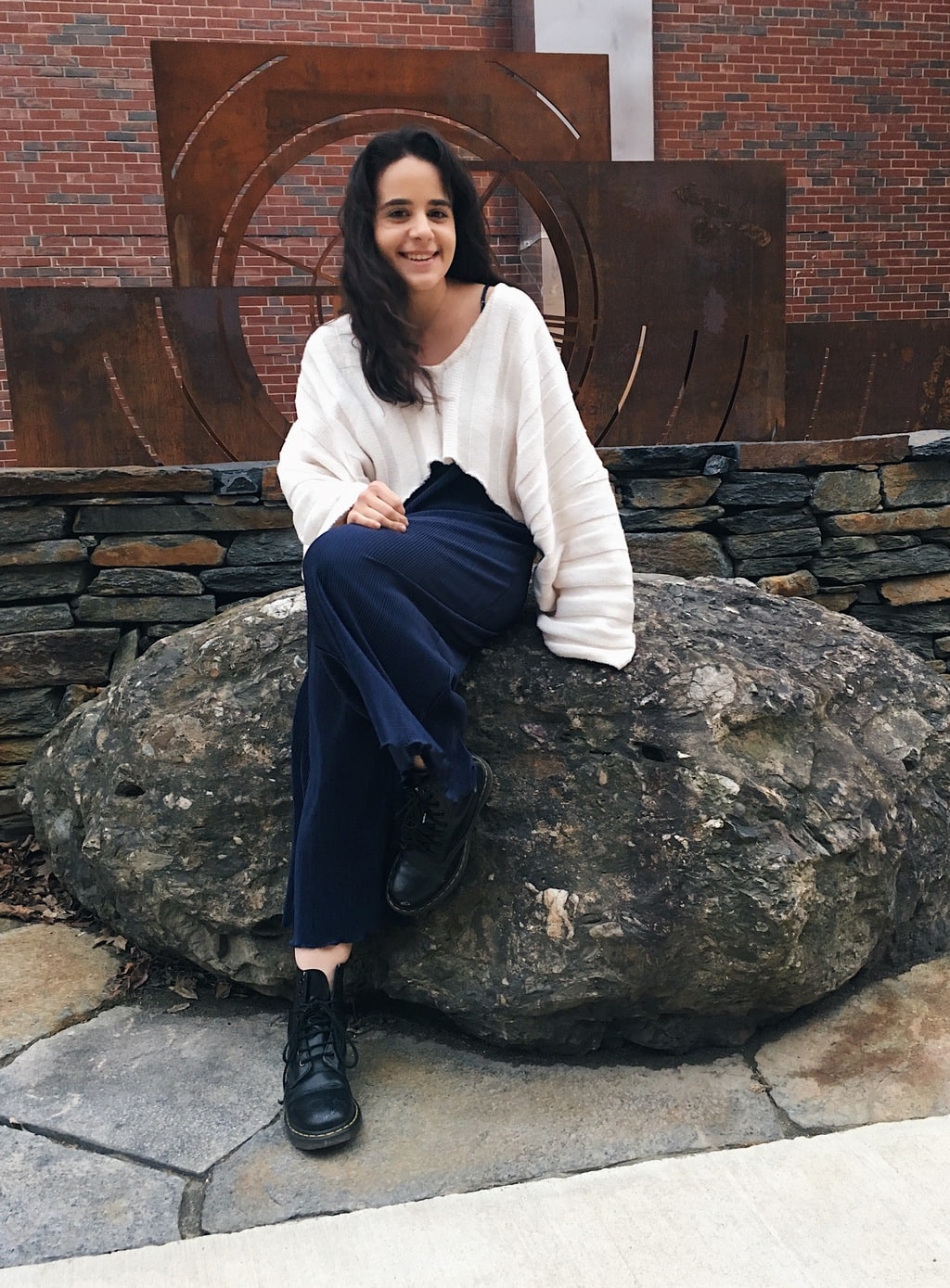 University of Massachusetts Amherst student Caeli sports a flowy navy blue jumpsuit, a loose-fitting, v-neck white cropped sweater, and some chunky black Doc Martens