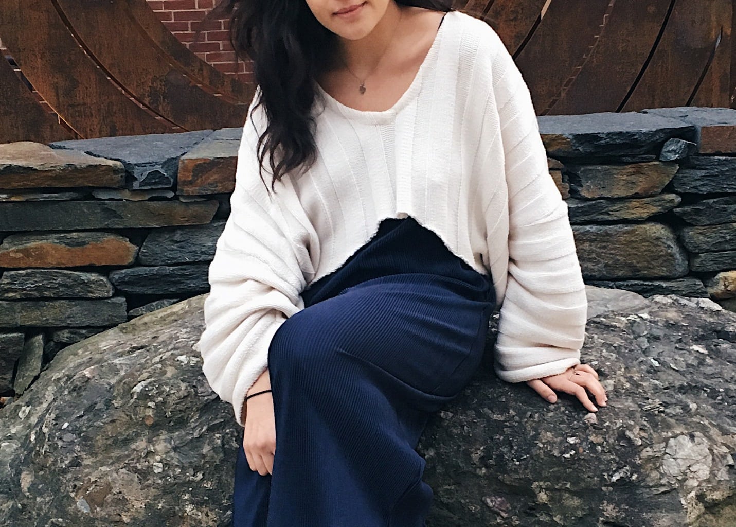 Caeli wears a loose-fitting white striped cropped sweater over a navy blue flowy jumpsuit.