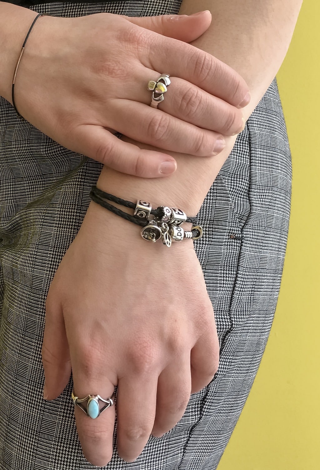 Caroline's simple silver jewelry all flows together. She wears a silver ring with a heart on it, black braided bracelets with silver charms, and a turquoise ring.