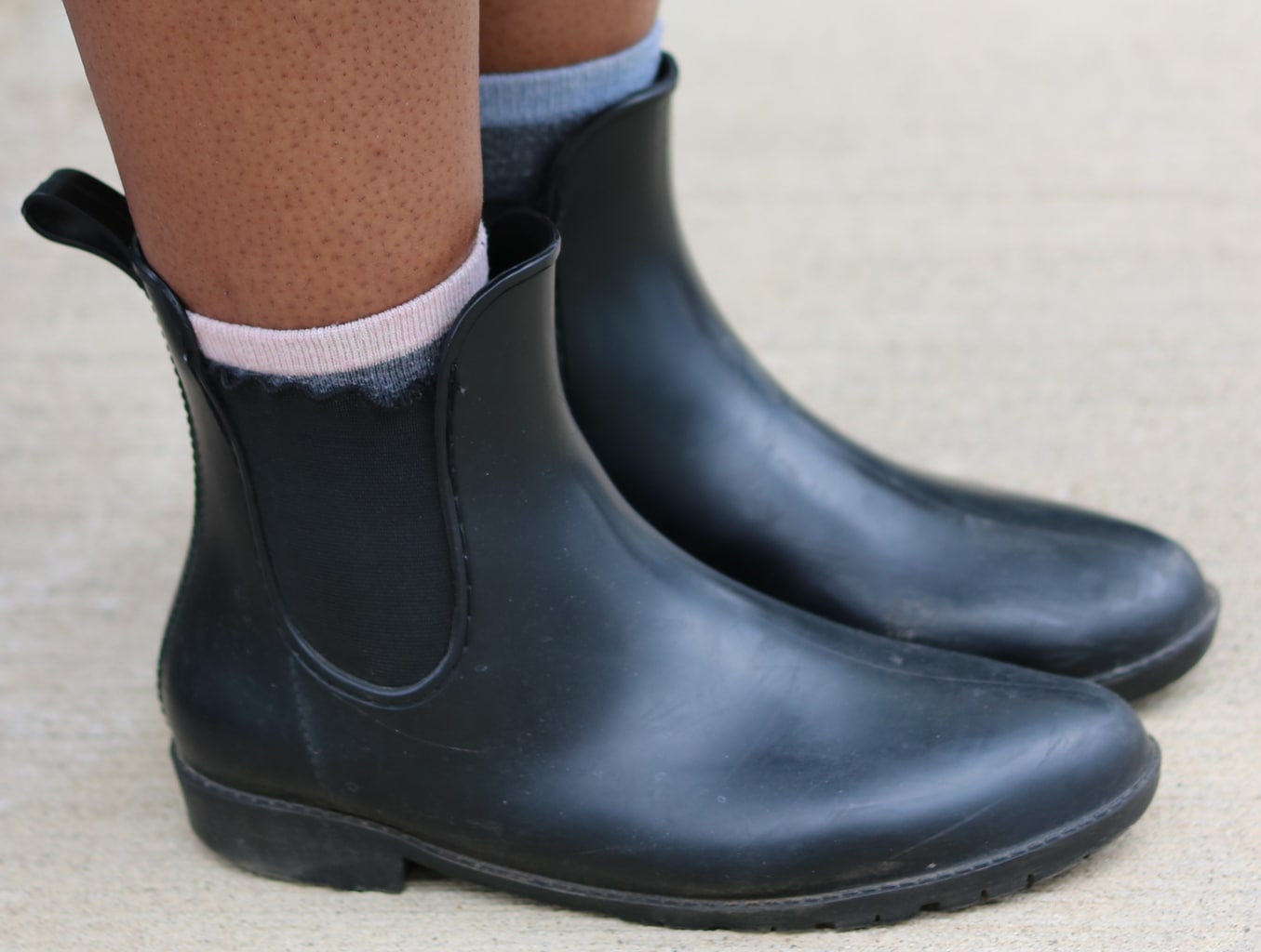 Cynthia wears flat black Chelsea rubber rain boots with different colored socks peeking out.