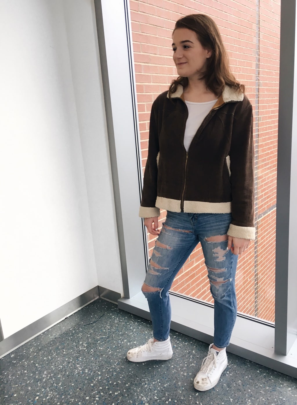 University of Massachusetts student Erin wears a brown corduroy jacket with shearling details, a white tee, ultra distressed denim jeans, and white Vans.