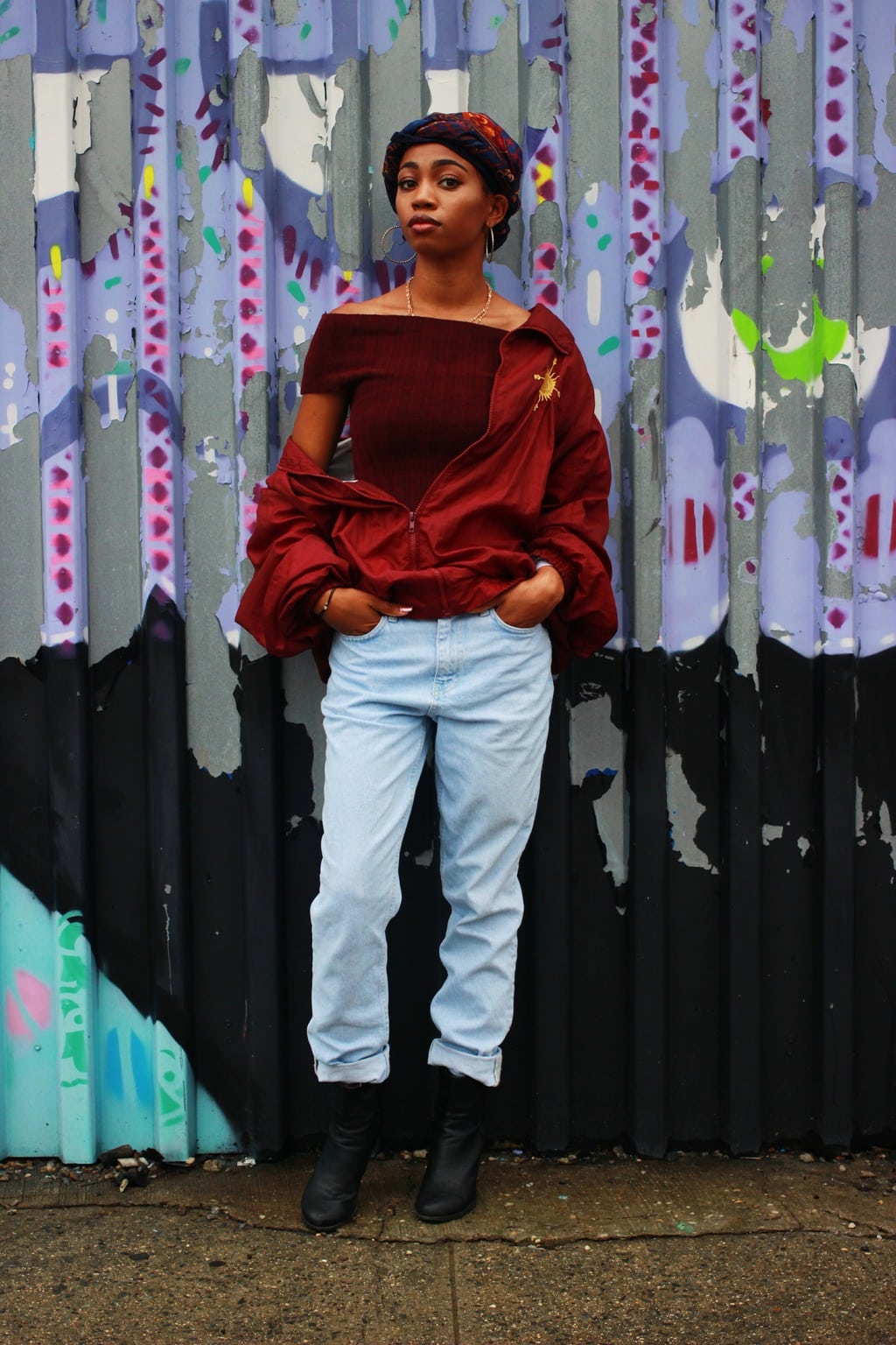 Student style; oxblood off-the-shoulder top, vintage windbreaker jacket, headscarf, distressed light-wash jeans, and chunky black booties.