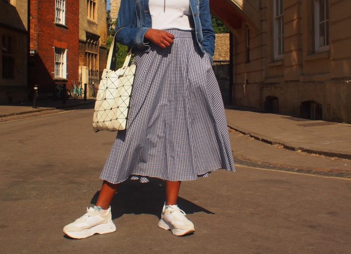 Chelsea wears a blue and white gingham midi circle skirt with chunky oversized white sneakers.