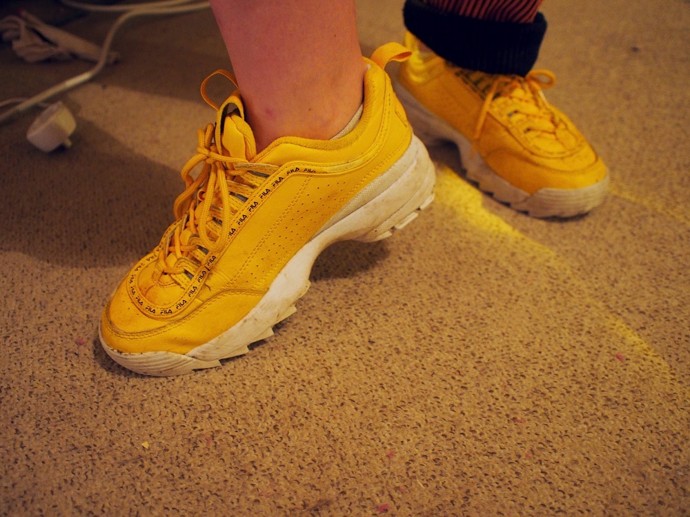 Martha wears chunky yellow sneakers with white soles and yellow laces.