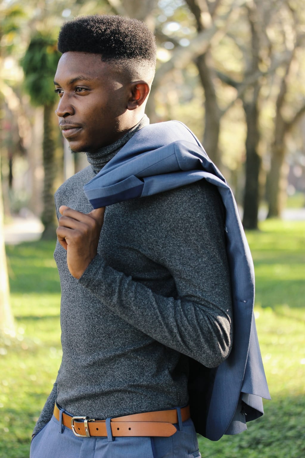 Adedamola wears a comfortable heather grey turtleneck tucked into blue slacks with a skinny tan belt.