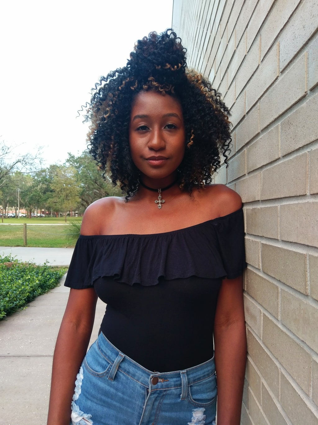 Payton wears an off-the-shoulder black ruffled bodysuit with cross choker necklace and a pair of light-wash denim jeans.