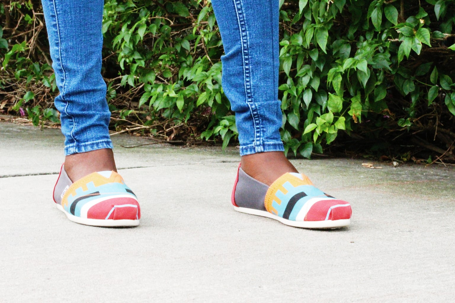 Uchoku wears bright blue, yellow, white, gray, and red Toms sneakers with straight-leg denim jeans.