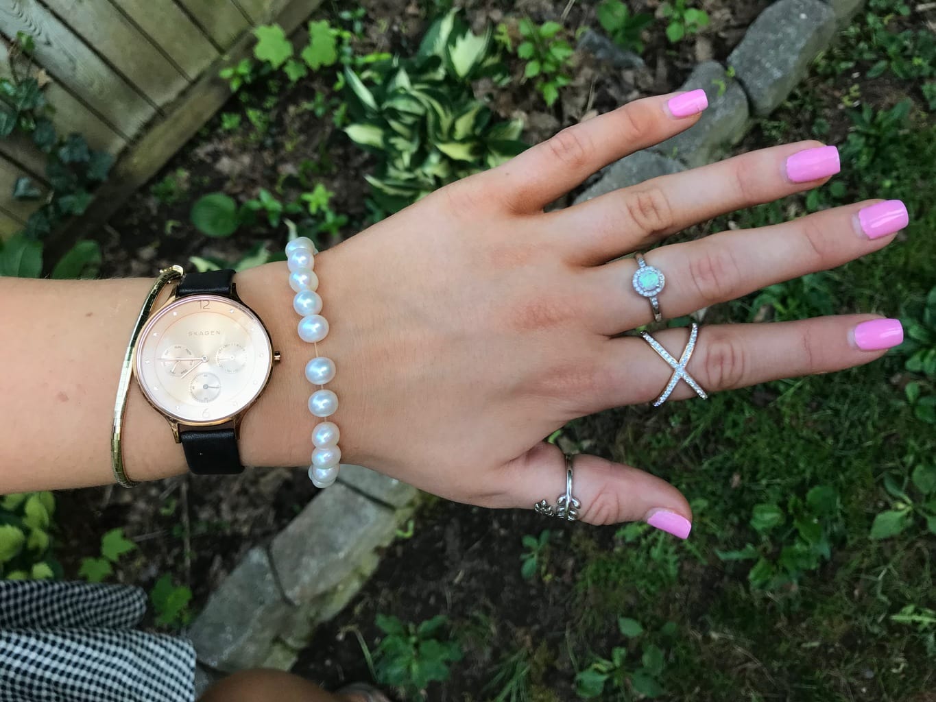 Madeline's arm candy consists of a delicate hammered gold bracelet, a rosegold watch with a white face and black straps, and a white pearl elastic bracelet. She also wears a silver wraparound vine ring, a crisscrossed X ring, and a ring with a blue gemstone.