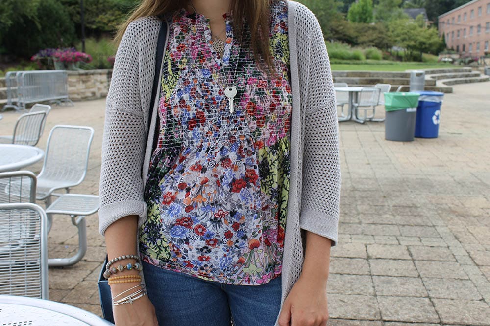 Alyssa wears a pink, blue, green, and white blouse with white stitching and a light grey open knit 3/4-length sleeve cardigan.