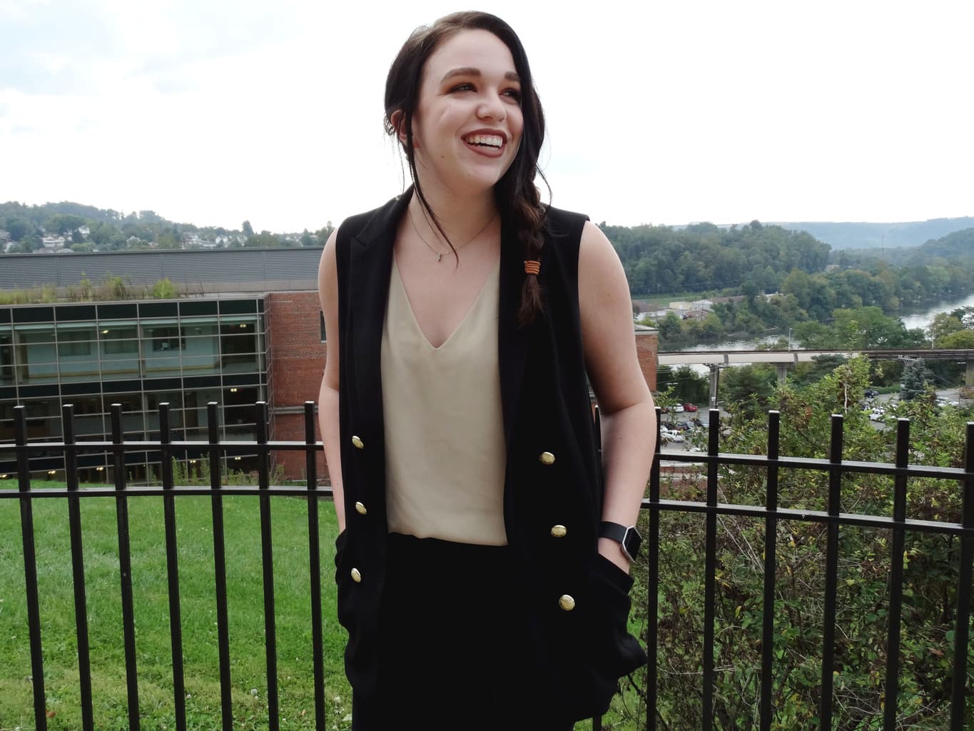 Bree wears a black military-style sleeveless vest with gold buttons and a tan tank top tucked into black trousers.