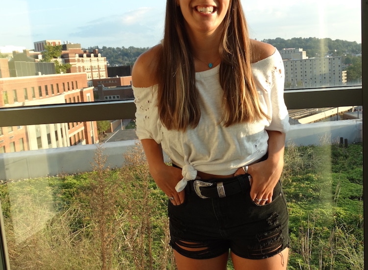 This off-the-shoulder white tee is tied to show off her high-waisted black distressed denim shorts and big silver belt buckle.