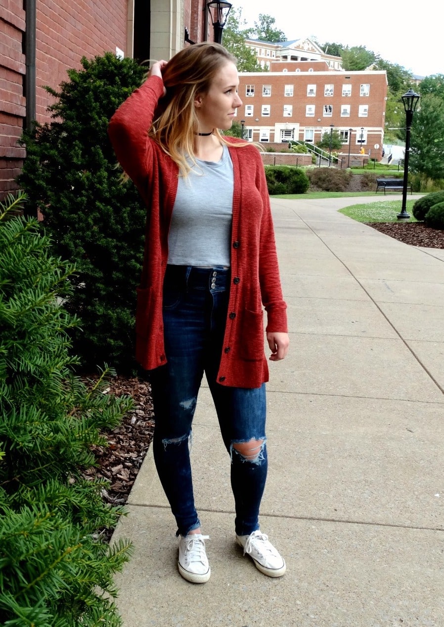 West Virginia University student stands out in a long red unbuttoned cardigan with a simple grey tee, distressed high-waisted dark denim jeans, Converse sneakers, and a black choker.