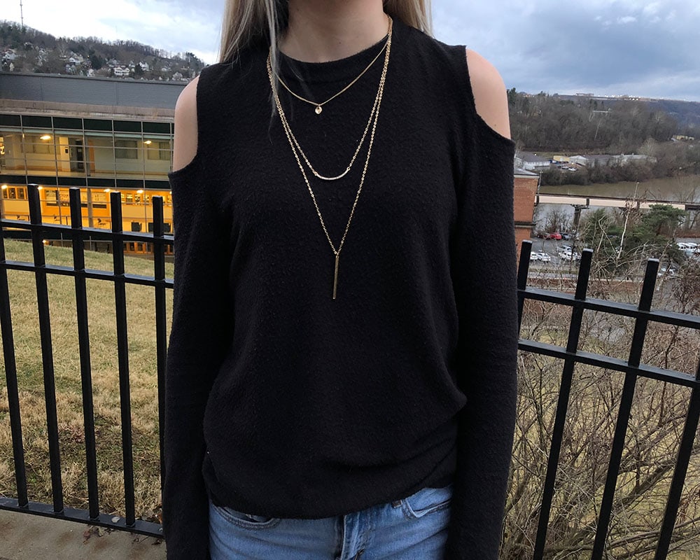 This black long-sleeve cold shoulder sweater is paired with a dainty gold layered necklace.