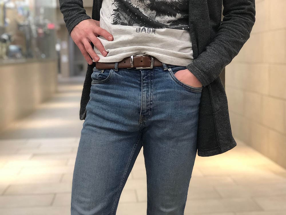 Davey wears medium-wash fitted denim jeans with a brown belt with a silver buckle.