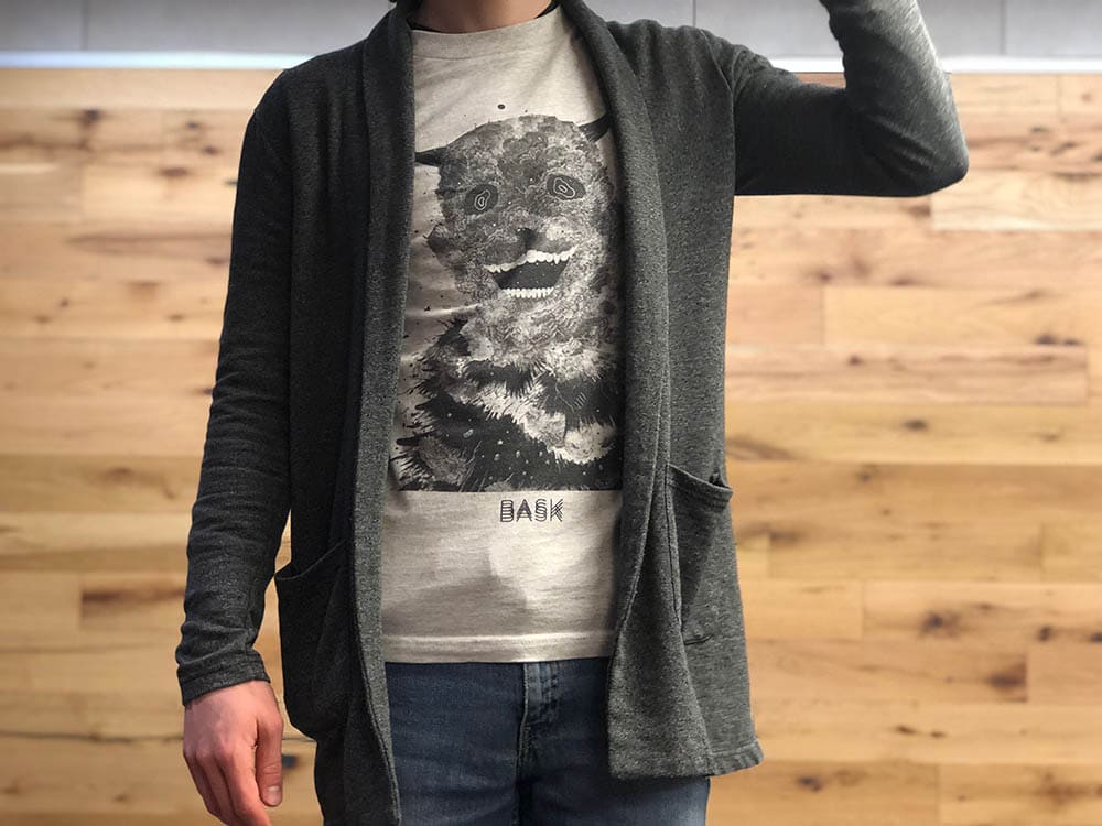 Davey wears a light grey graphic tee with a long-sleeve dark grey cardigan with pockets.