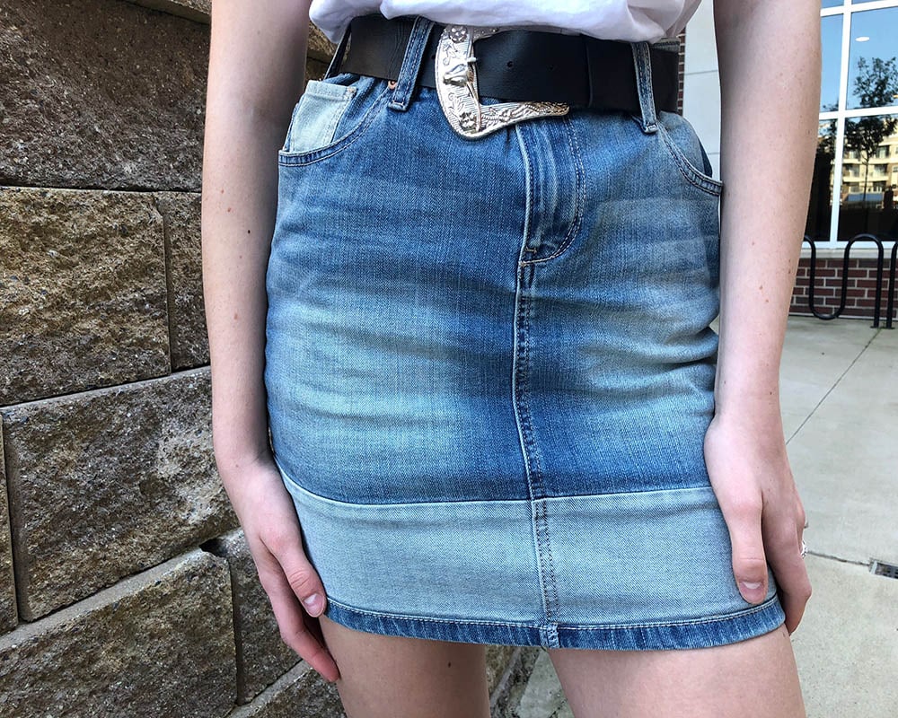 Emily's two-toned denim patchwork skirt is high waisted and held up by a thick black belt with a silver Western style buckle.
