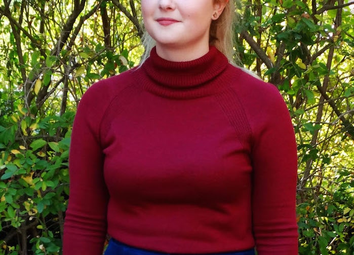 Emma tucks her wine-colored burgundy turtleneck sweater into a blue high-waisted skirt.