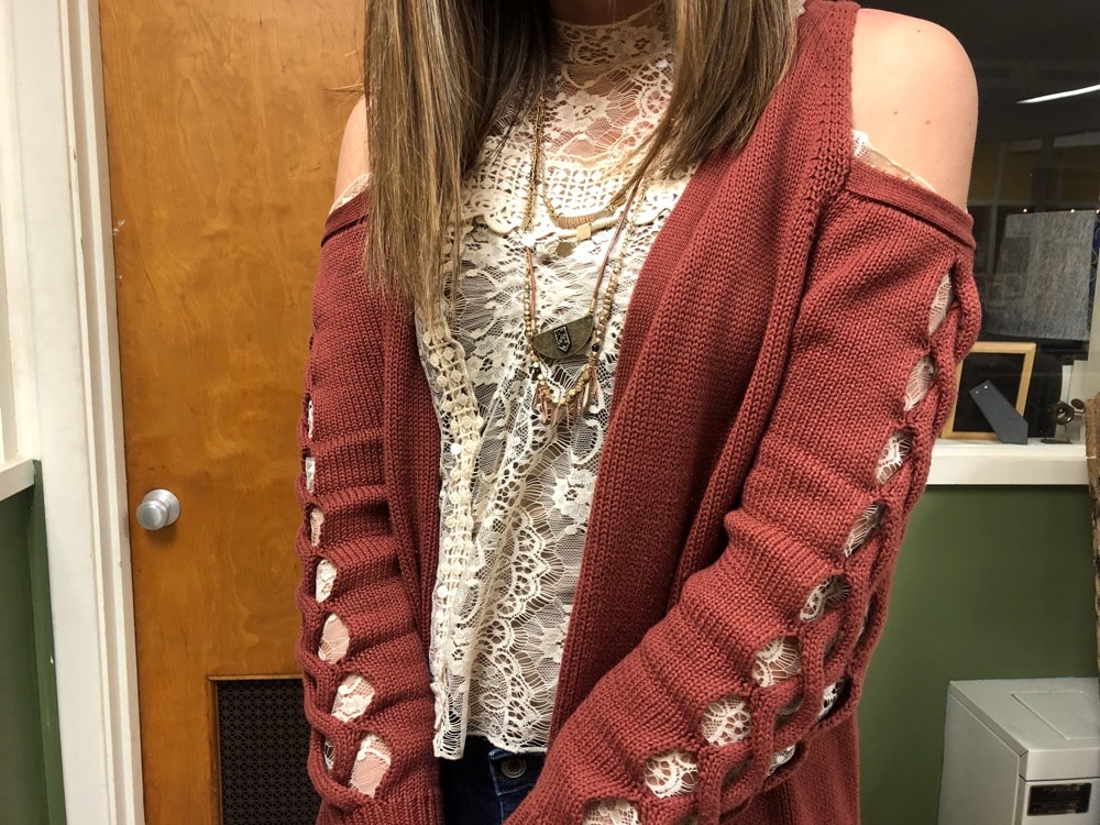 Gentry pairs her cream high neck blouse with a burnt sienna red sweater with open shoulders and cut sleeves.