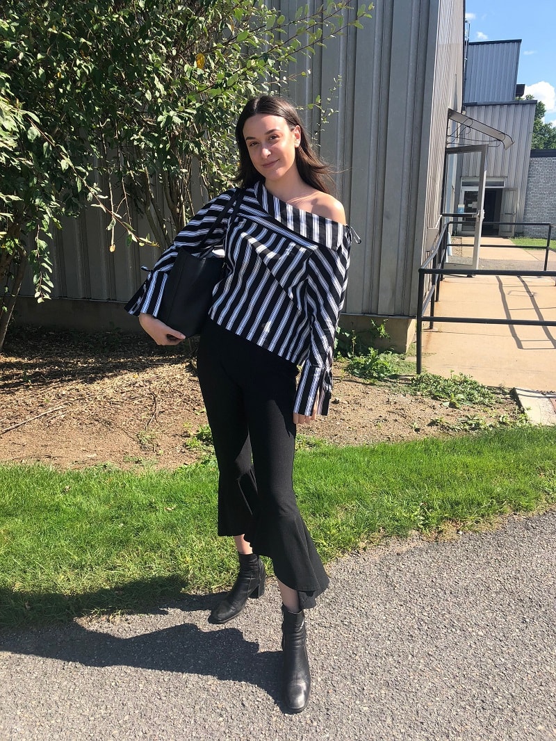 West Virginia University student Georgia wears a striped off-the-shoulder black and white blouse with bell sleeves, black cropped flare trousers, and black chunky heeled boots.