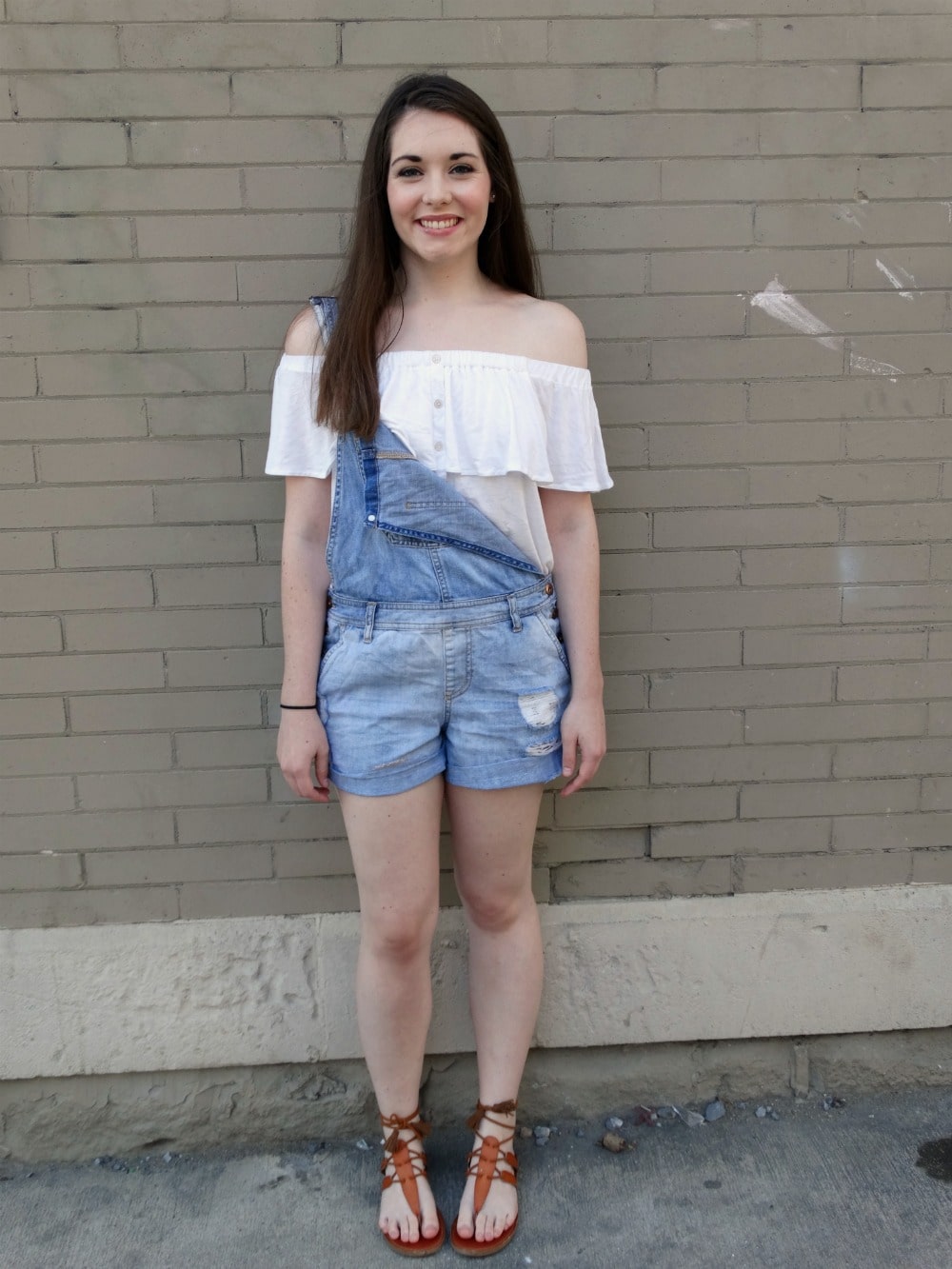 College student at West Virginia University wears an off-the-shoulder top with overall shorts for casual summer style.