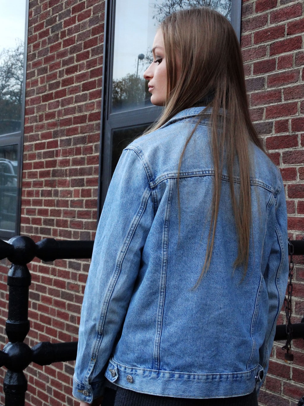 Kayse sports an oversized distressed denim jacket with a dark grey turtleneck sweater underneath.