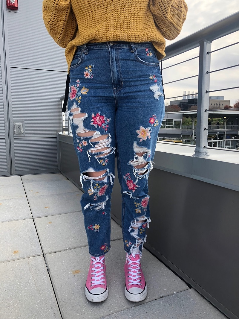 Maria's high-waisted jeans are ripped and embroidered with colorful flowers.