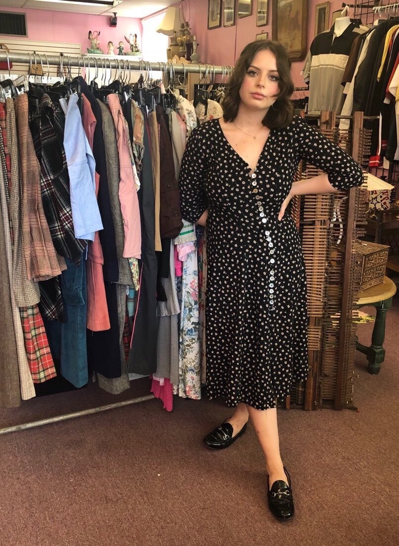 Mary wears a vintage, black button-down midi-length dress with 3/4 length sleeves and shiny pearl buttons and black leather loafers.