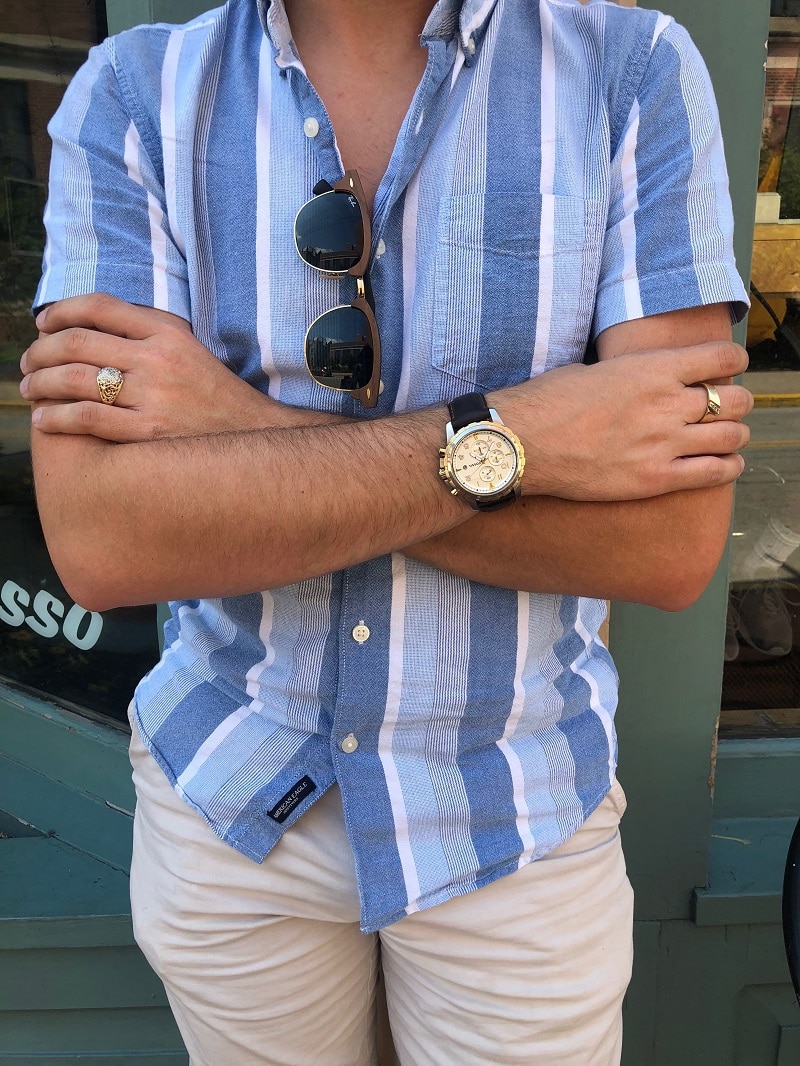 Nathan pairs his blue button-up shirt with hand-me-down silver rings, a large-face Fossil watch with a dark brown leather band, and Ray-Ban Clubmasters.