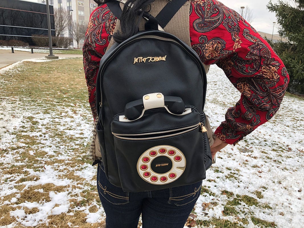 This vintage phone backpack adds charm to Teddy's look. It is black with a rotary phone detailing and a front pocket.