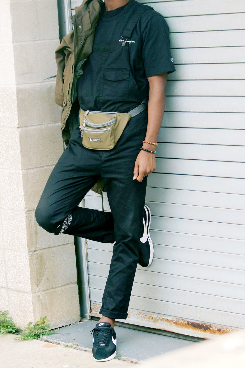 Men's fashion at University of South Florida: Student Karon sports a light brown fanny pack with a black Champion tee and black overalls. He wears a bandana around his leg.