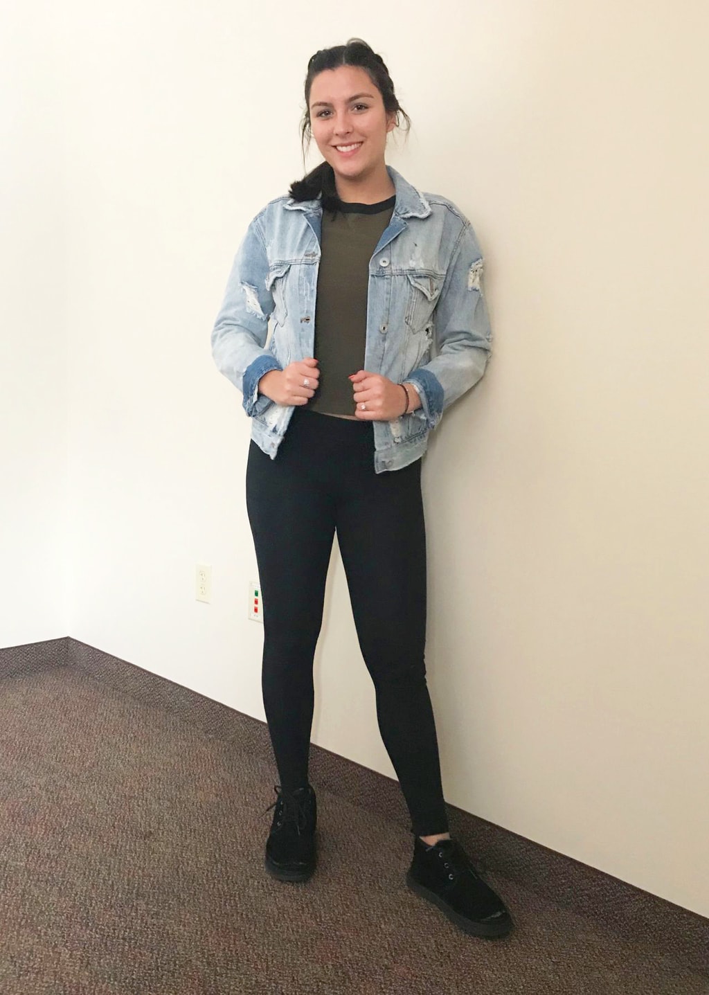 Mercyhurst fashion: Mercyhurst University student Arianna looks is comfortable in her olive green crop top with a black neckline, light-wash distressed denim jacket with the cuffs rolled up, black leggings, and black casual lace-up sneakers.