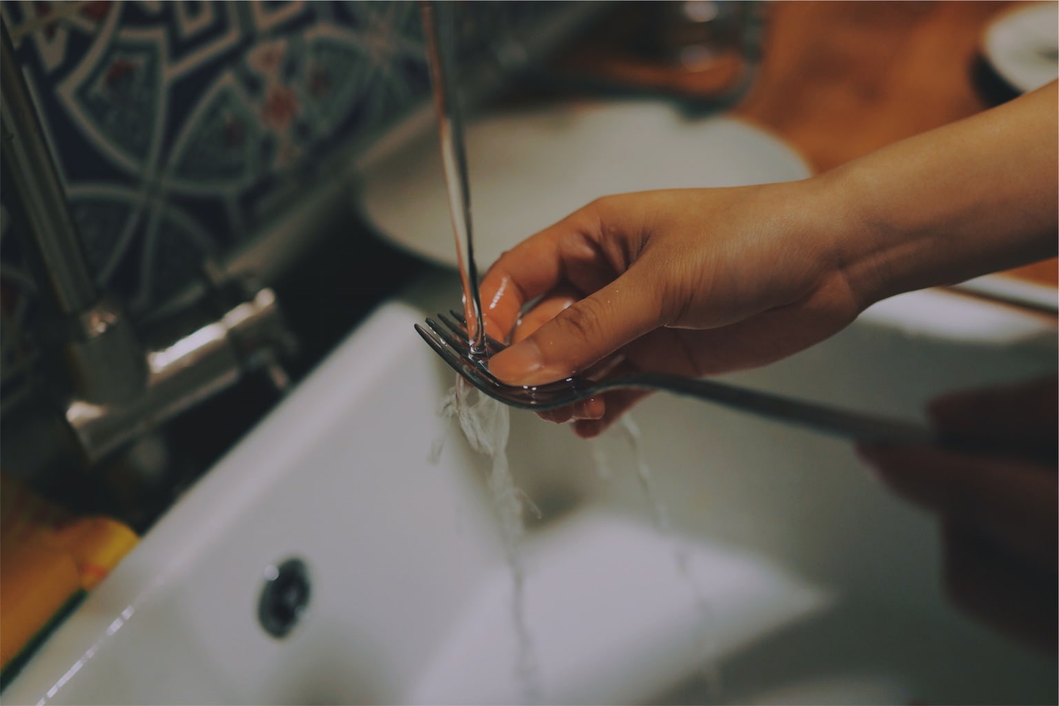 Shot of someone's hand washing a fork in a sink, doing dishes