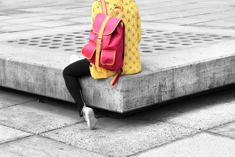 Women sitting on public bench with bright red backpack