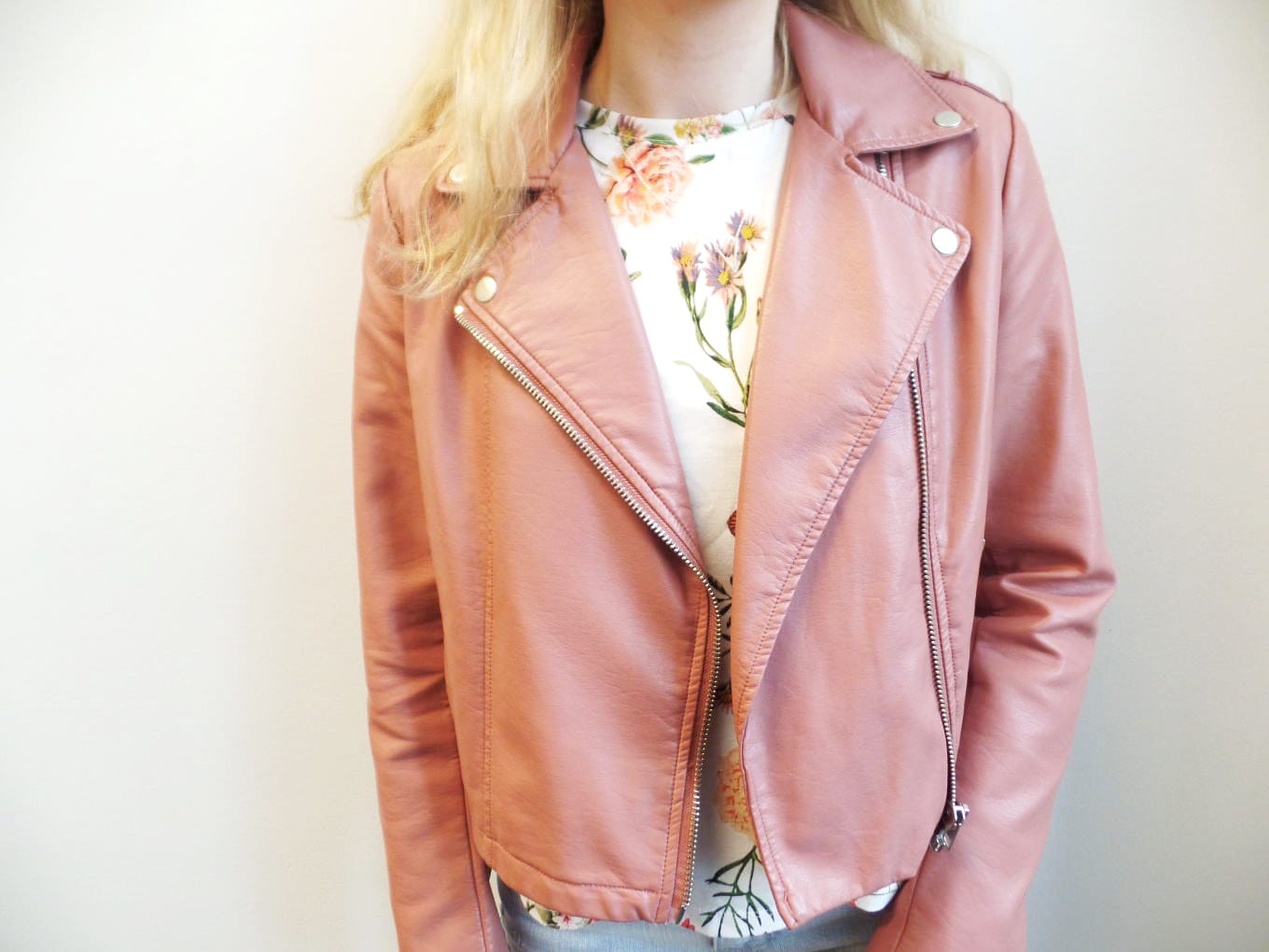 Veronica wears a dusty rose faux leather motorcycle jacket with a white floral shirt.