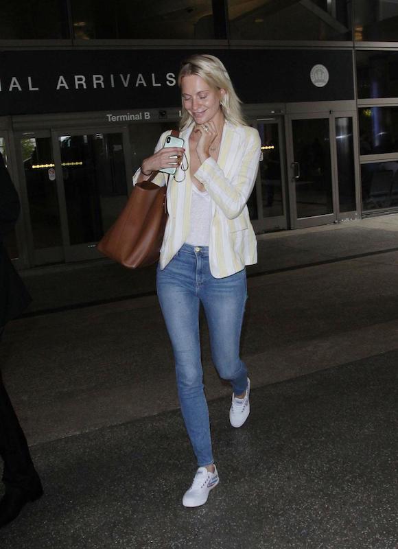 Poppy Delevingne wearing a yellow and white striped blazer, a white t-shirt, skinny jeans, a brown oversized tote bag, and white low-top sneakers