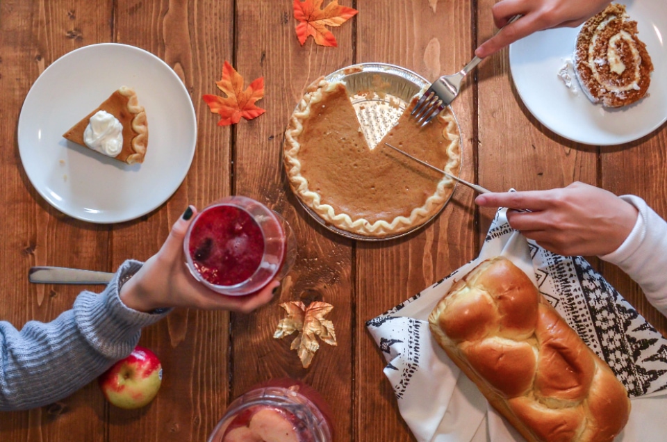 Woman cutting into pumpkin pie with bread, drinks, and dessert for Thanksgiving