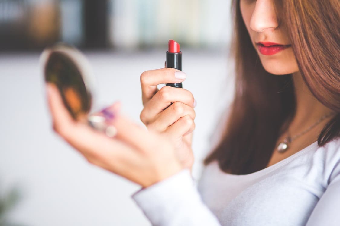 girl wearing red lipstick holding lipstick and mirror