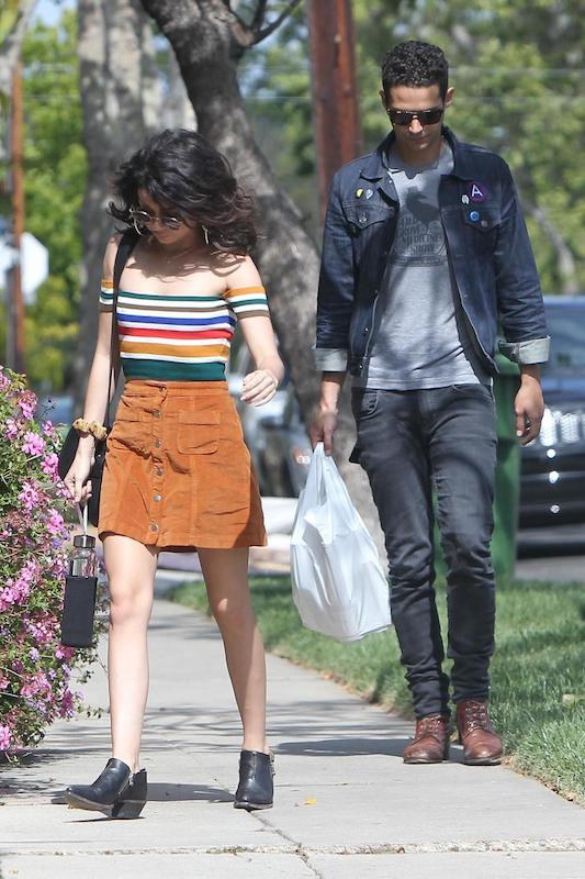 Sarah Hyland wearing a rainbow striped off the shoulder top, a button front corduroy skirt, hoop earrings, round sunglasses, and black ankle booties